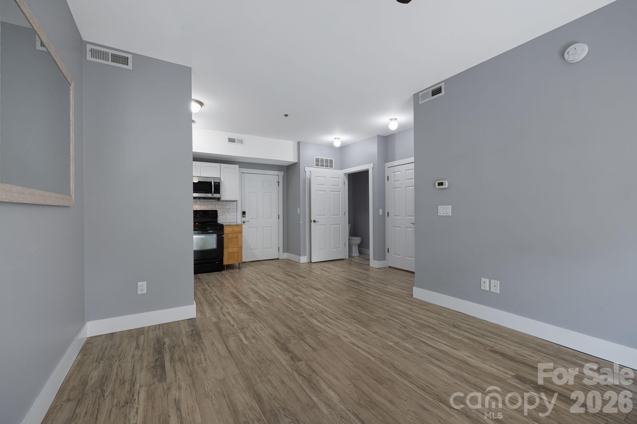 Vacant living area with wood-look flooring, gray walls, and a compact kitchen at the back.
