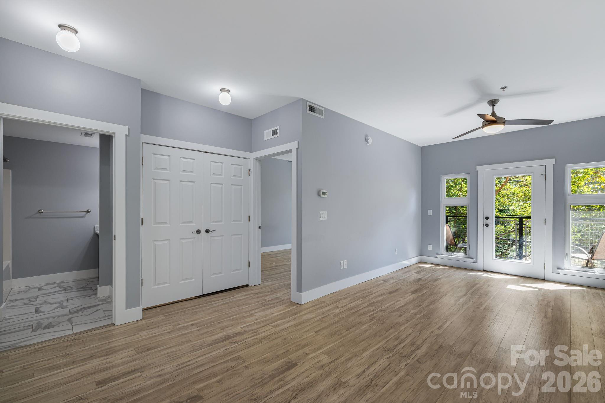 Unfurnished condo living room with wood-look floors and glass doors to a leafy balcony.