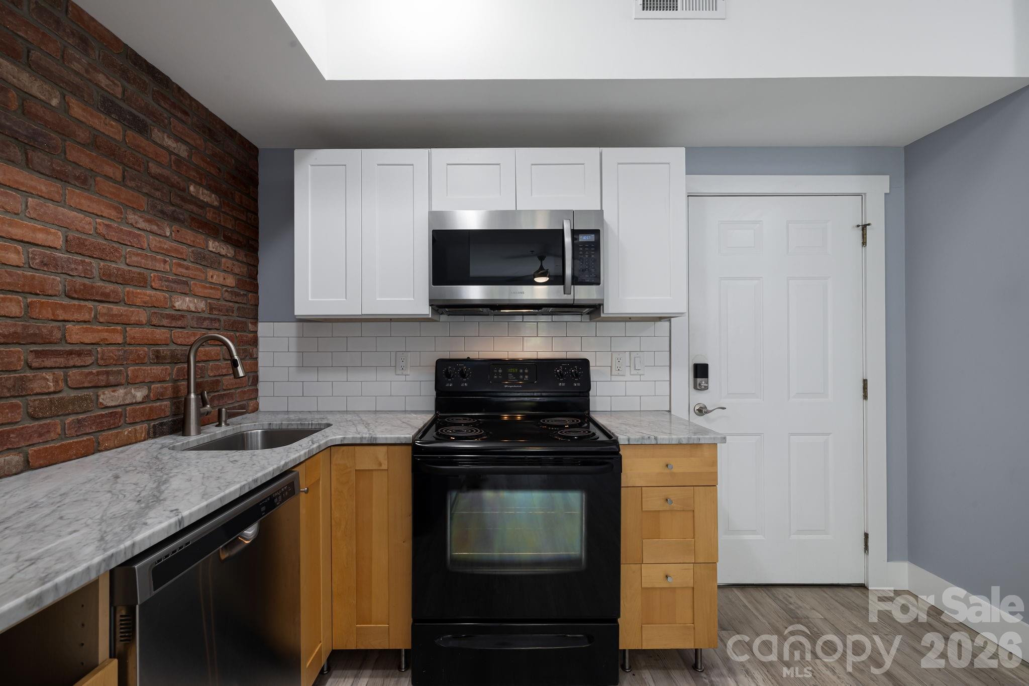 Kitchen with a brick accent wall, marble-pattern counters, and black range beneath a stainless steel microwave.