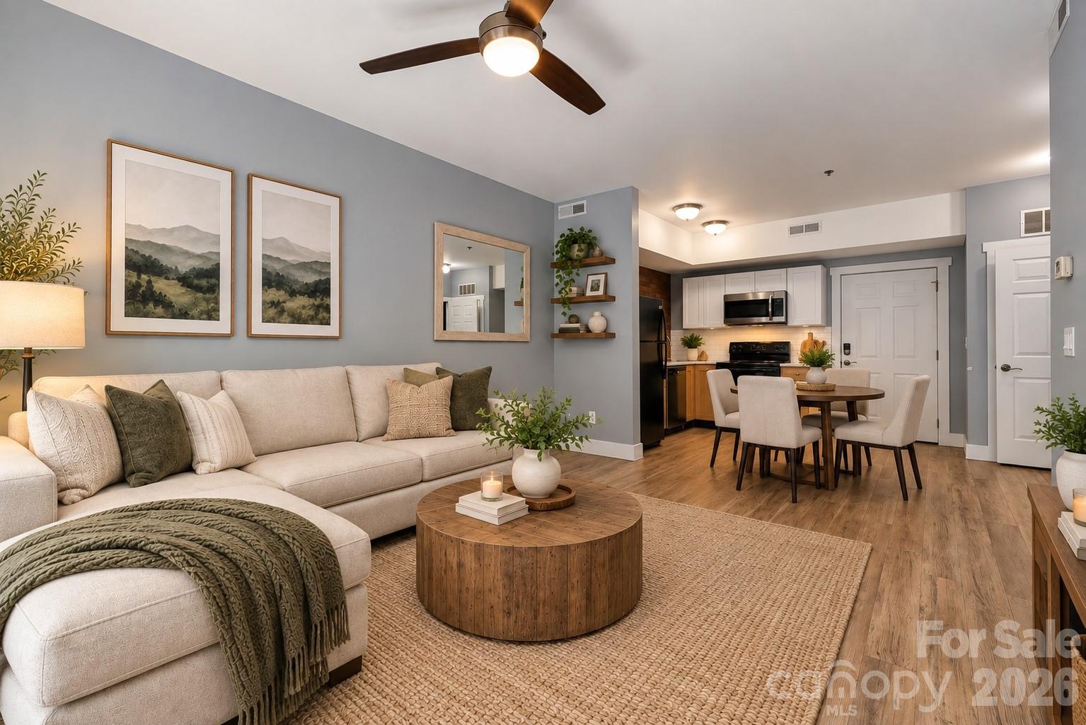 Open-plan condo living room with a cream sectional, round wood coffee table, and adjoining kitchen and dining area.