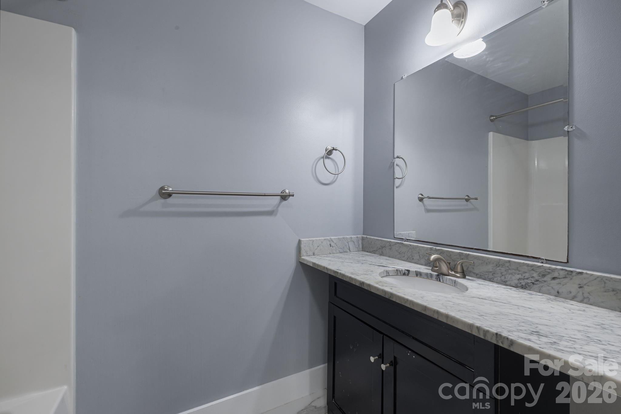 Bathroom with a marble vanity, dark cabinets, large mirror, and tub or shower enclosure.