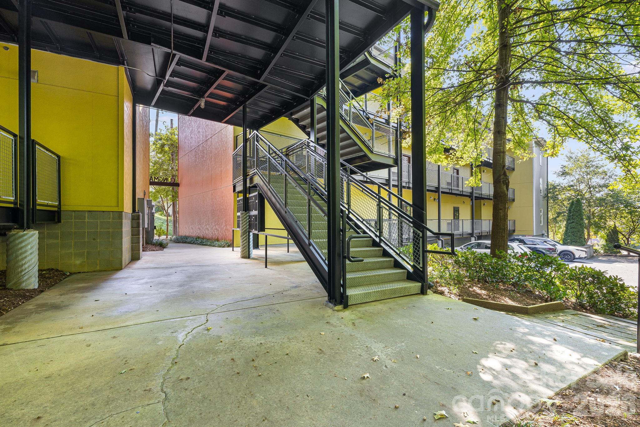 Apartment building exterior with black metal stairs, yellow walls, and a covered walkway.