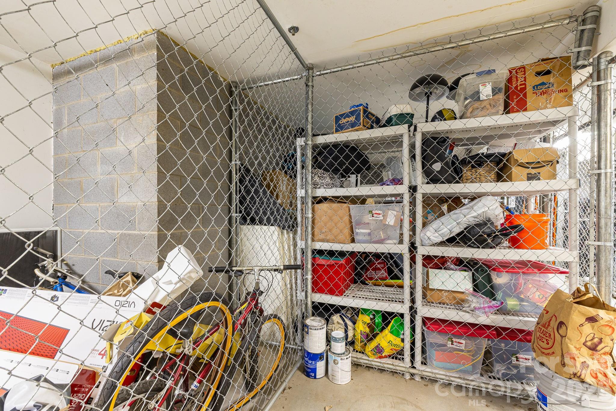 Caged storage area with mesh fencing, packed shelves, and bicycles.