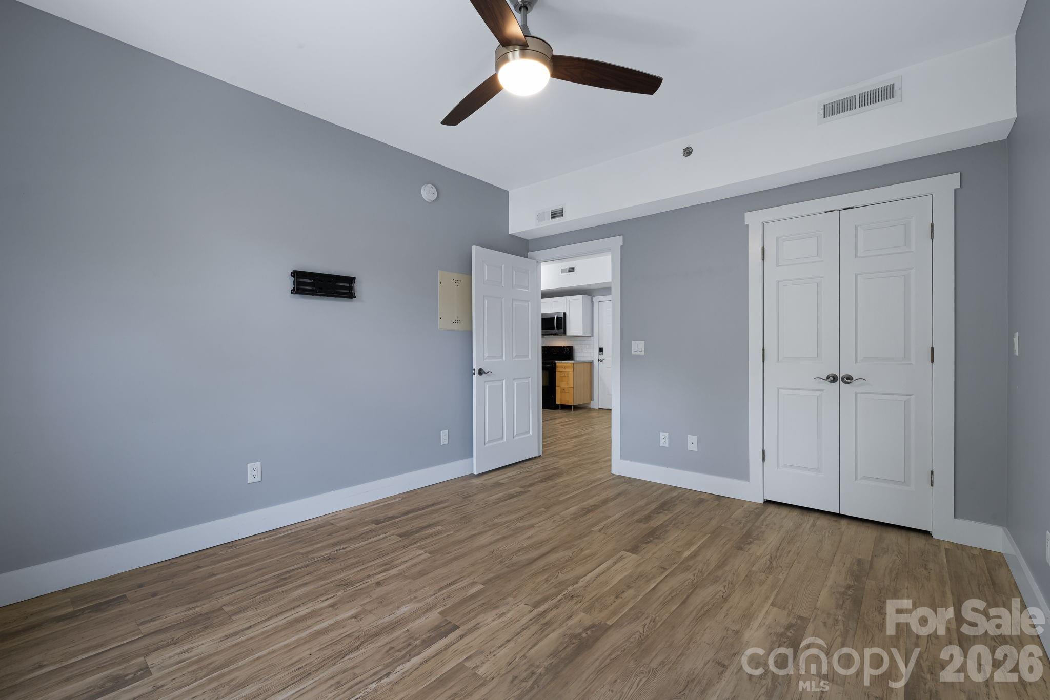 Empty bedroom with gray walls, wood-look floors, ceiling fan, and double closet doors.