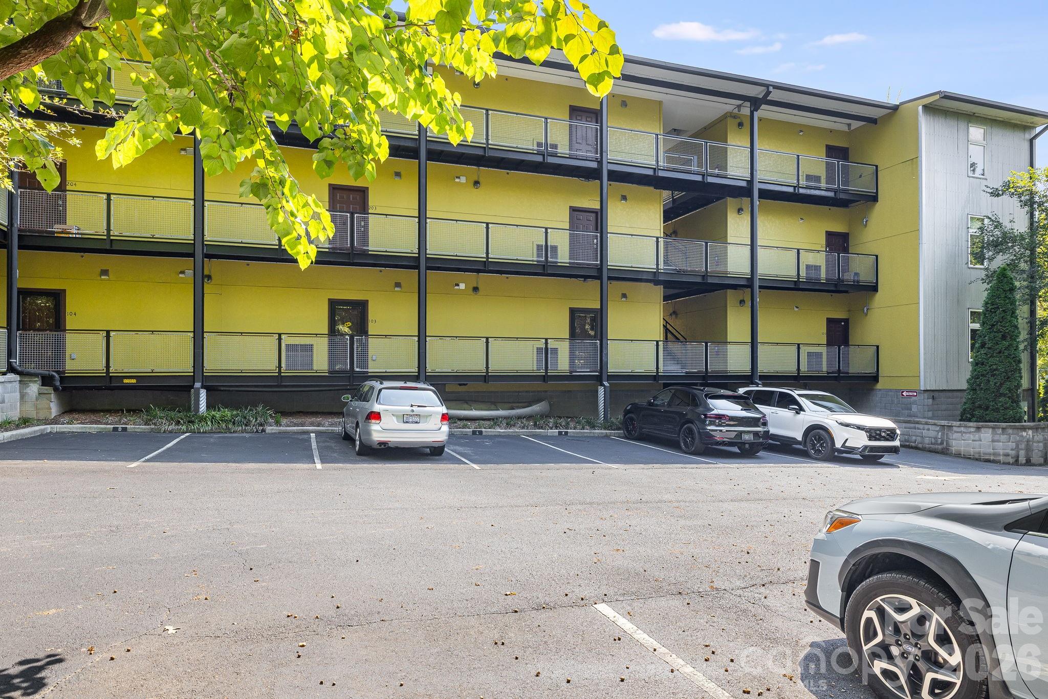 Yellow multi-story residential building with black-railed walkways and a parking lot in front.