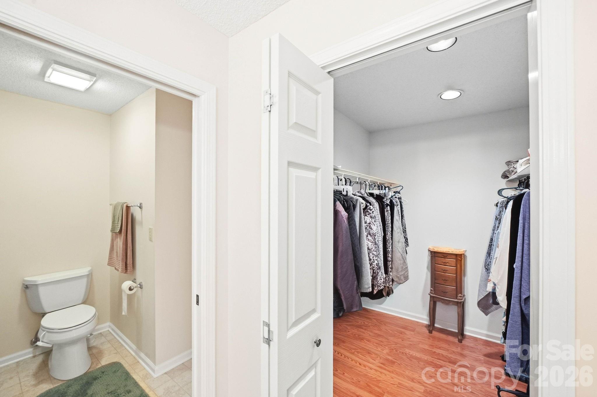 Walk-in closet with clothes along both sides and an adjoining toilet room.