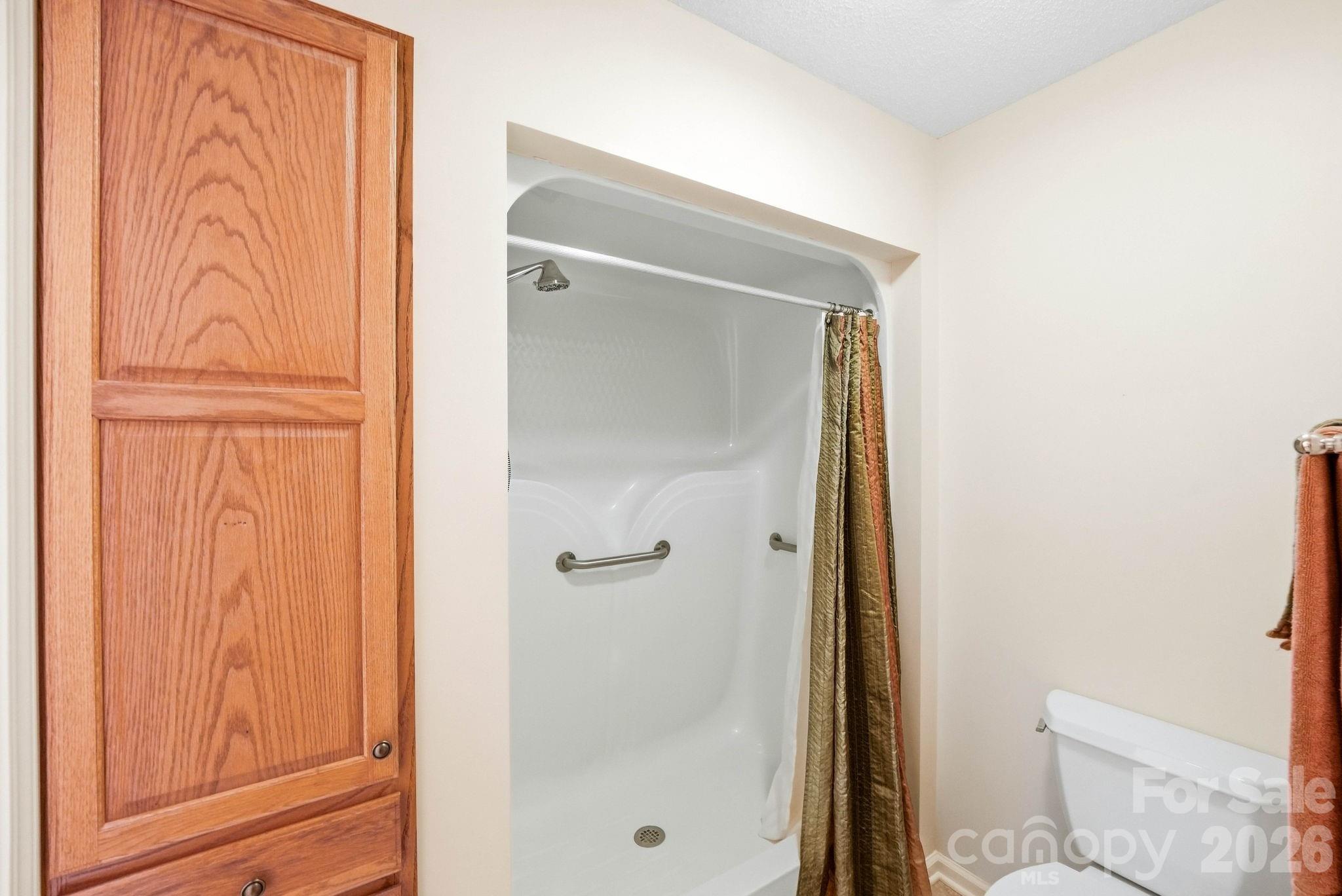 Bathroom with a white shower enclosure, grab bars, and oak cabinet.