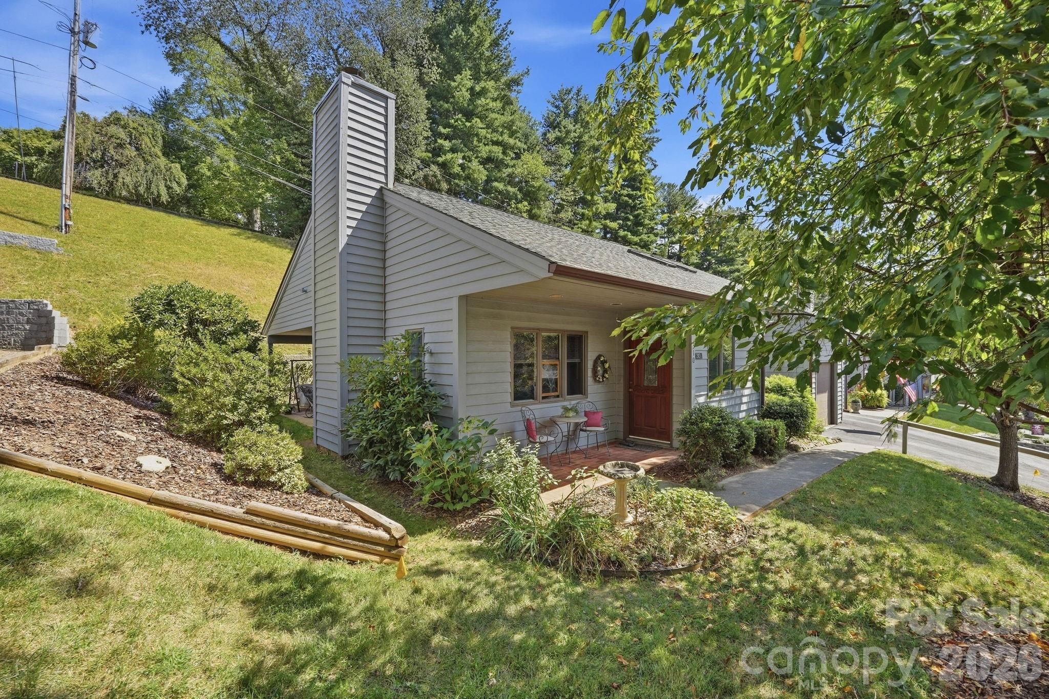 Gray-sided home with a tall chimney, covered porch, and landscaped sloping yard.