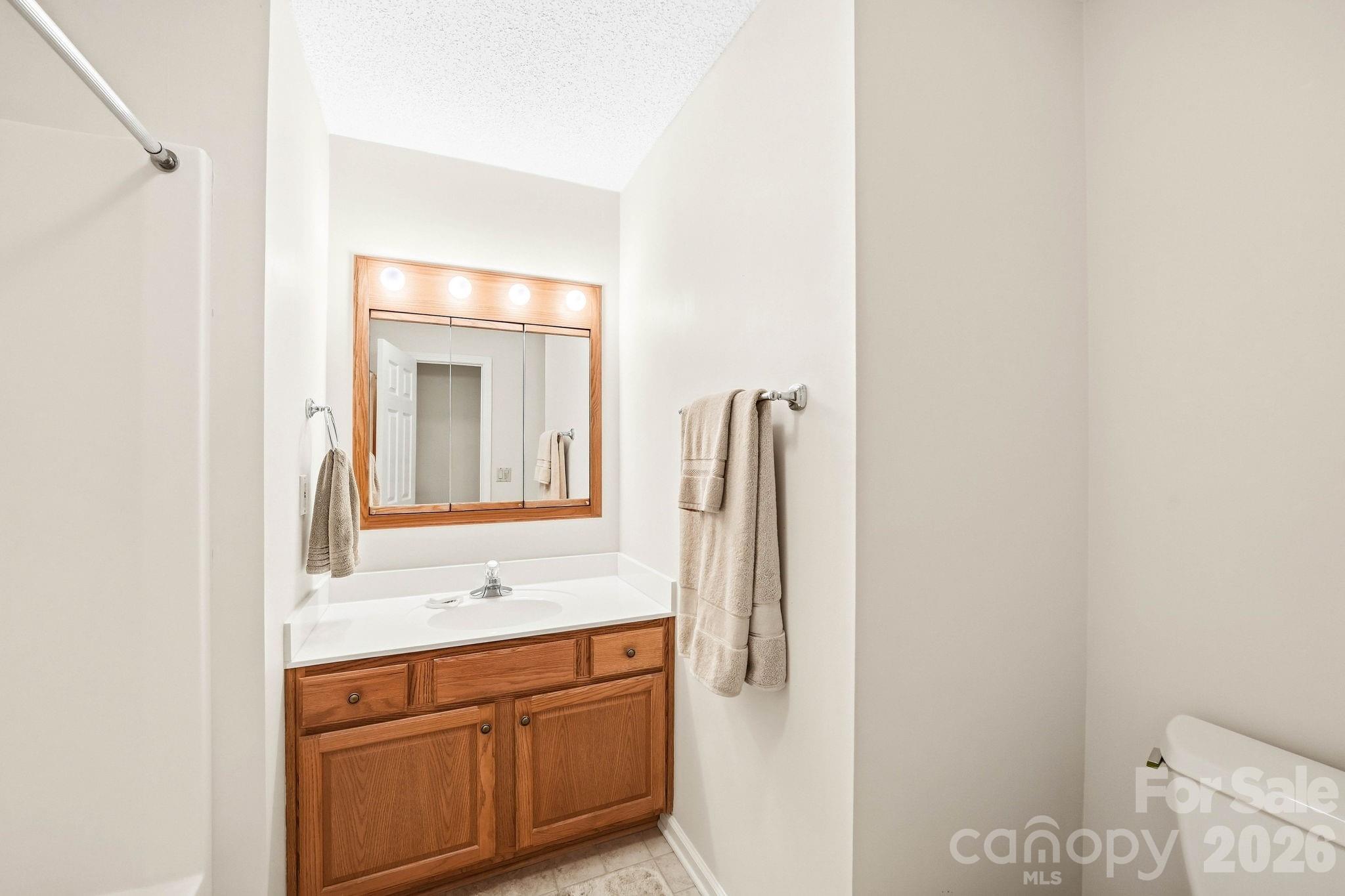 Bathroom vanity with a wood cabinet, white sink, mirrored medicine cabinet, and towels.