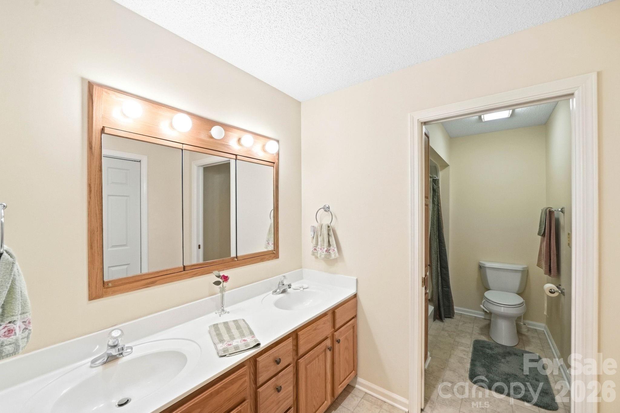 Bathroom with a double-sink wood vanity and an adjoining toilet room.