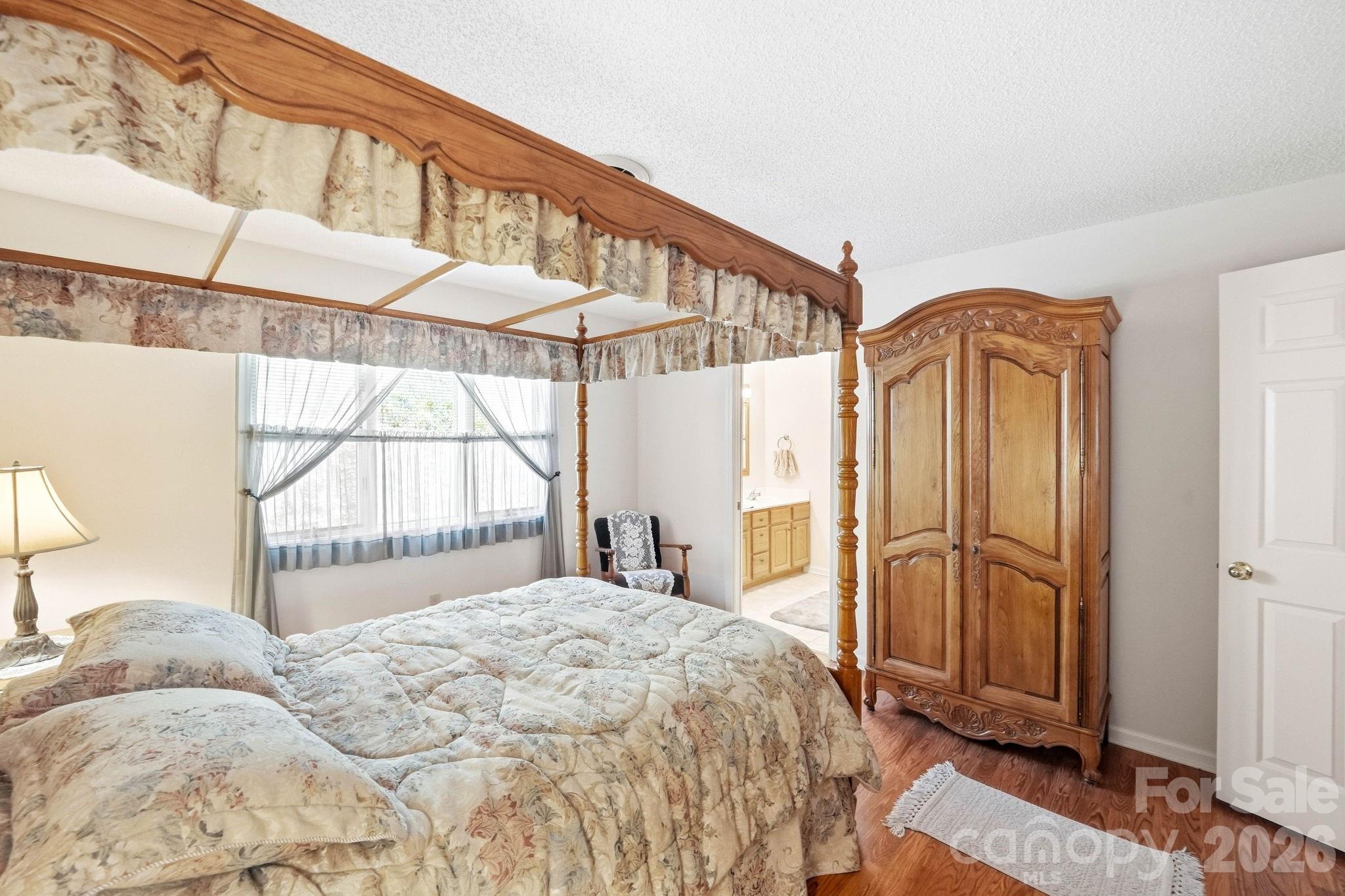 Bedroom with floral four-poster bed, carved wooden wardrobe, and adjoining bathroom vanity.