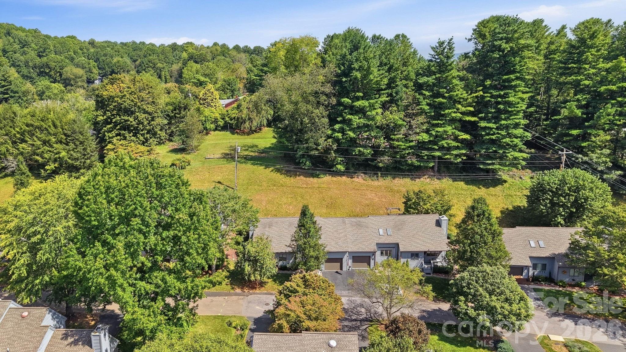 Aerial view of a gray-roofed home beside a broad lawn and mature trees.