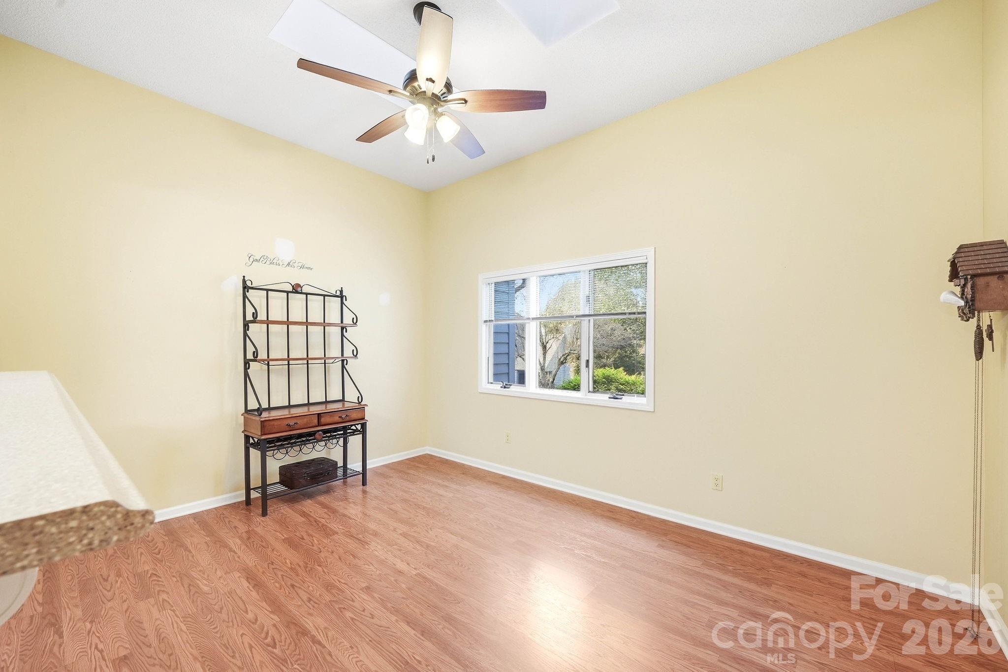 Bright room with hardwood floors, a ceiling fan, and a window overlooking greenery.