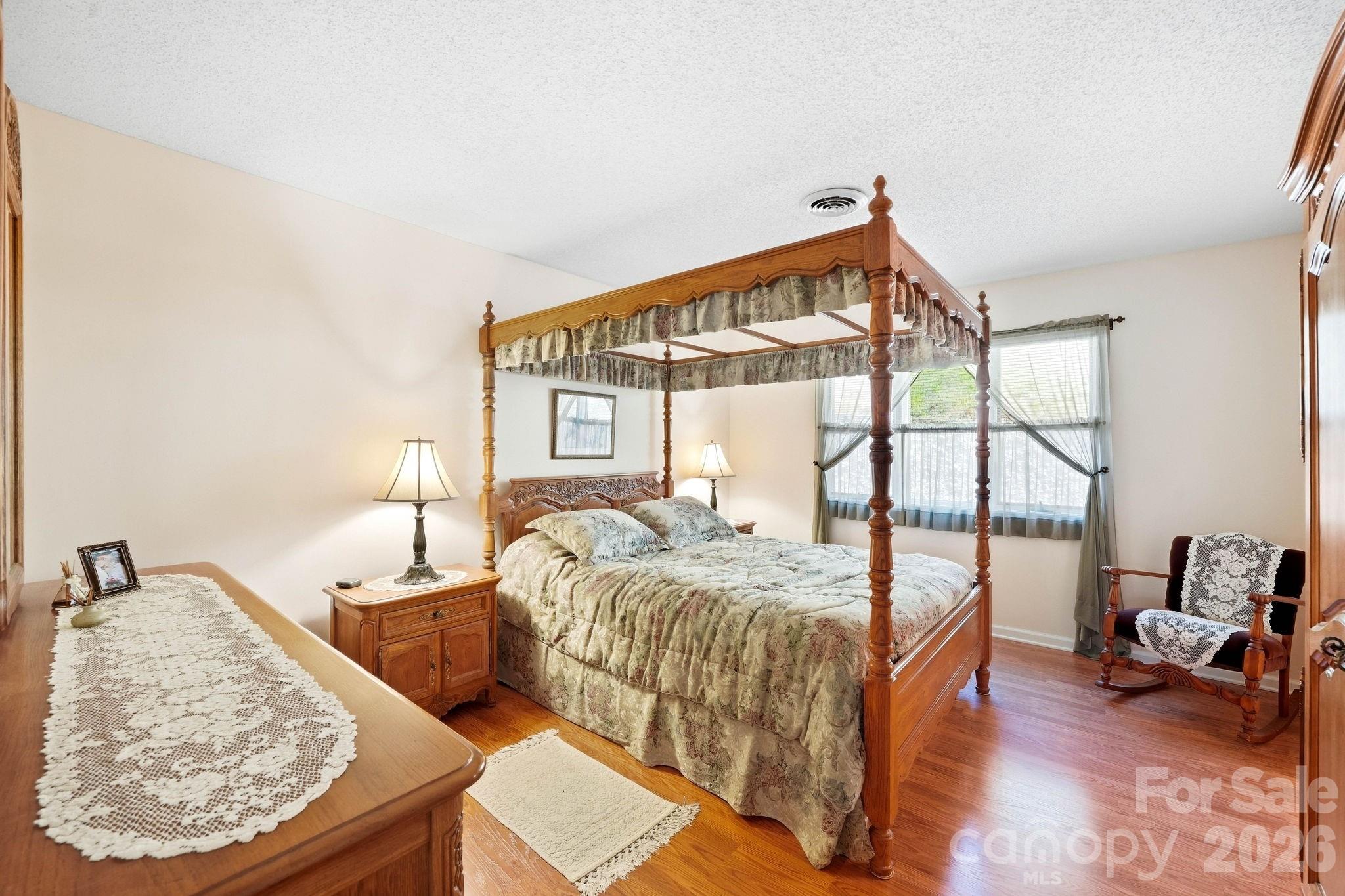 Furnished bedroom with a wooden four-poster canopy bed, floral bedding, and hardwood floors.