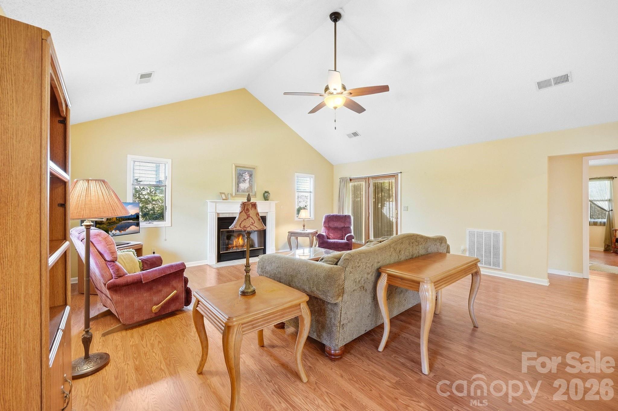 Living room with a vaulted ceiling, fireplace, and wood floors, furnished with a sofa and recliners.