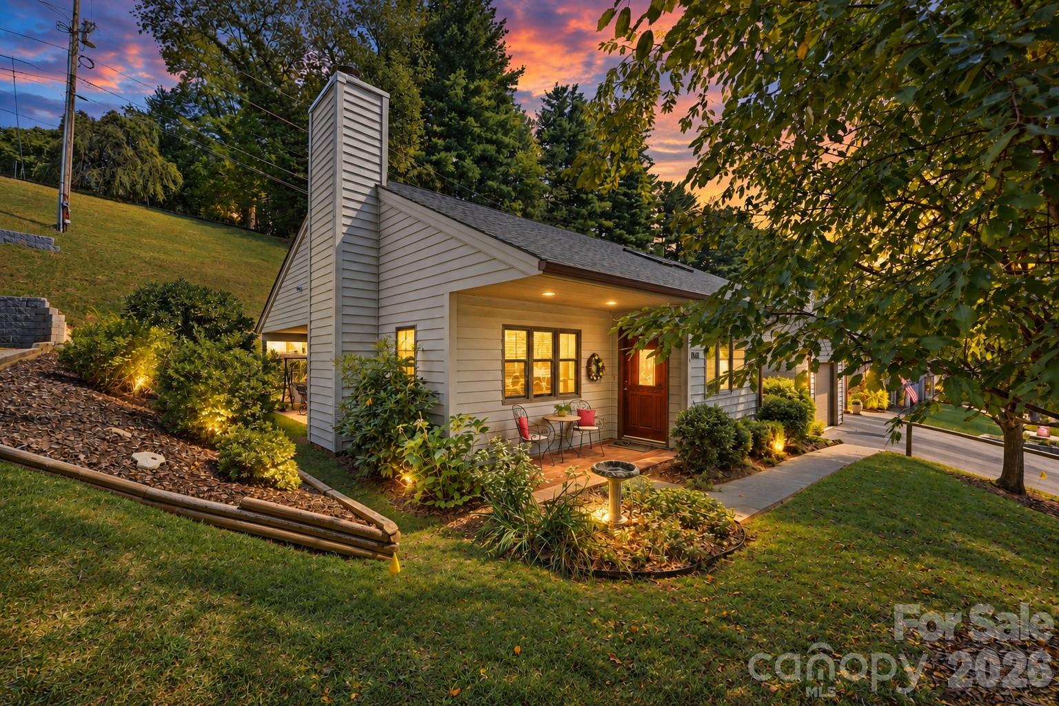 Light-sided home with a tall chimney and illuminated front porch at dusk.