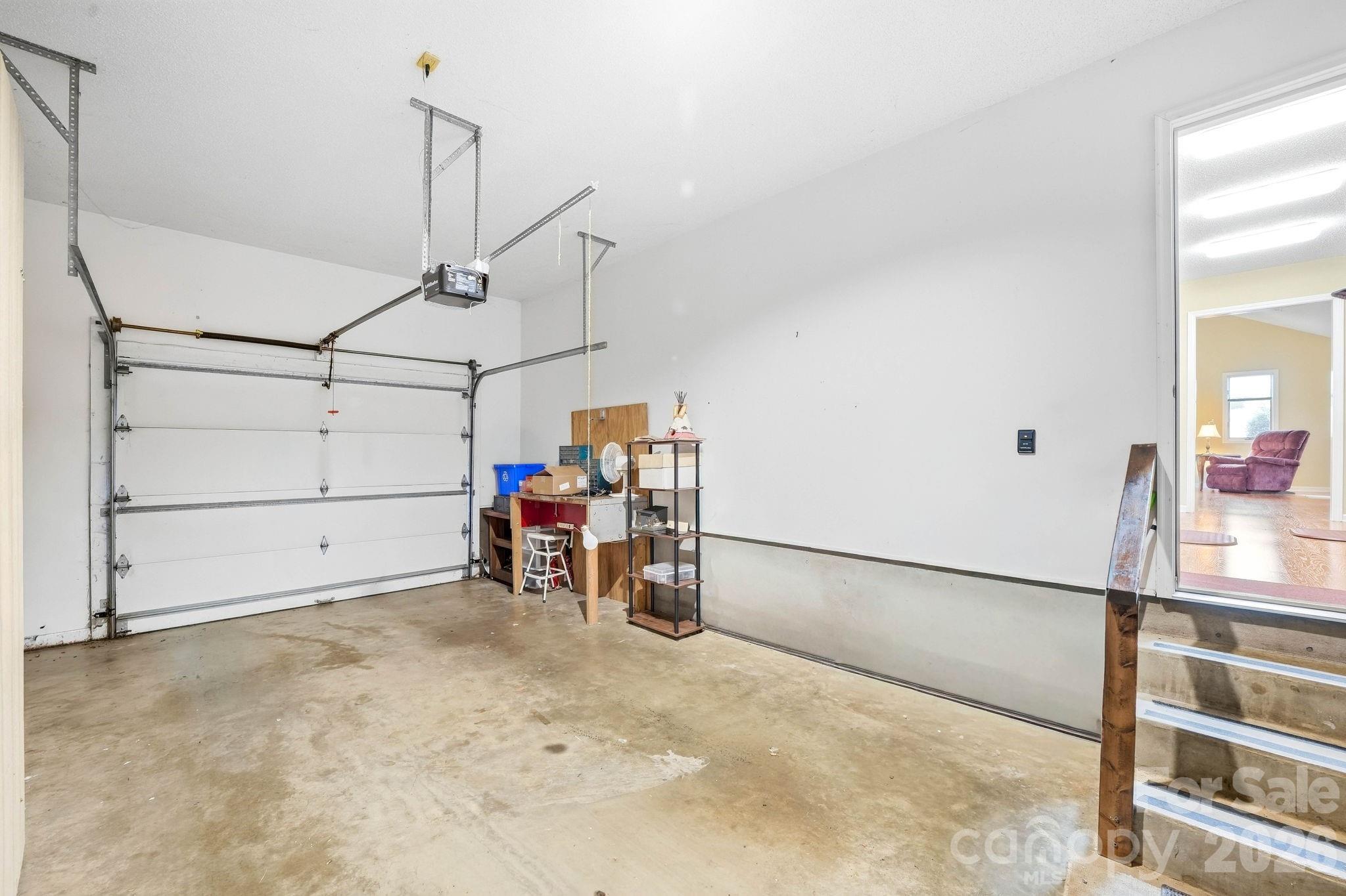 Garage with a concrete floor, overhead door, and workbench beside an open doorway to a furnished room.