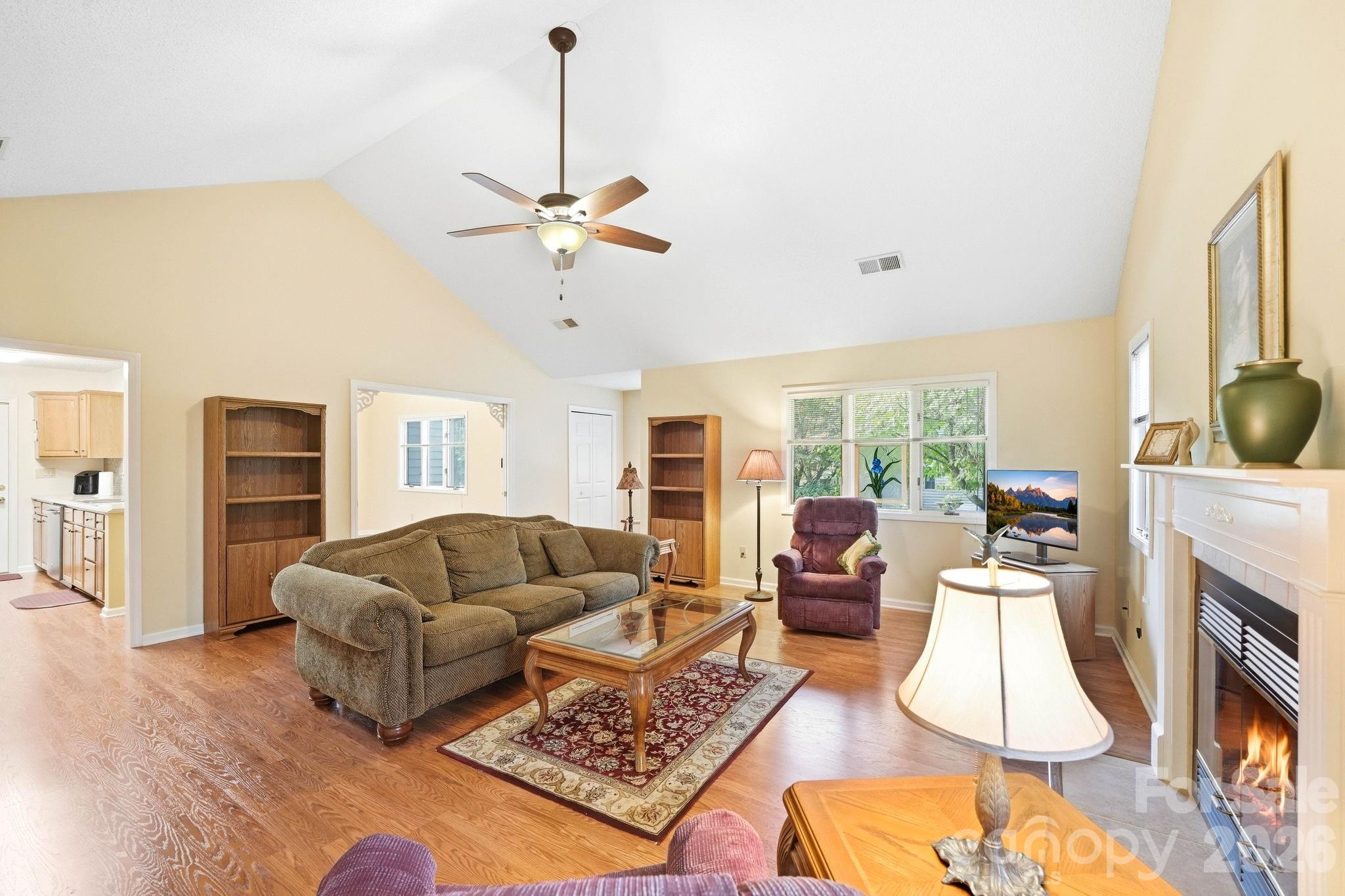 Living room with vaulted ceiling, hardwood floors, large windows, and a fireplace.