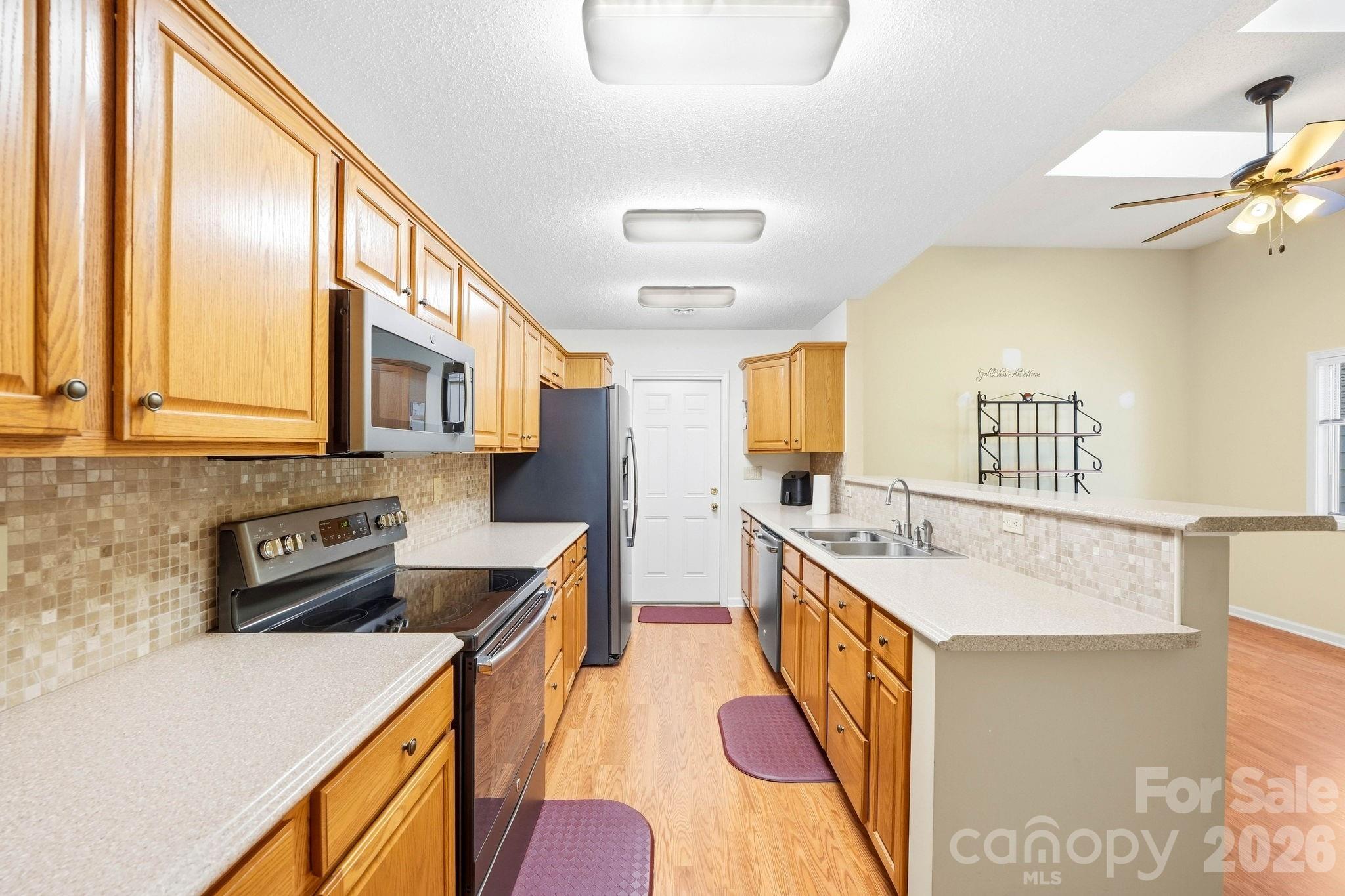 Galley kitchen with honey-colored cabinets, tiled backsplash, and stainless steel appliances.