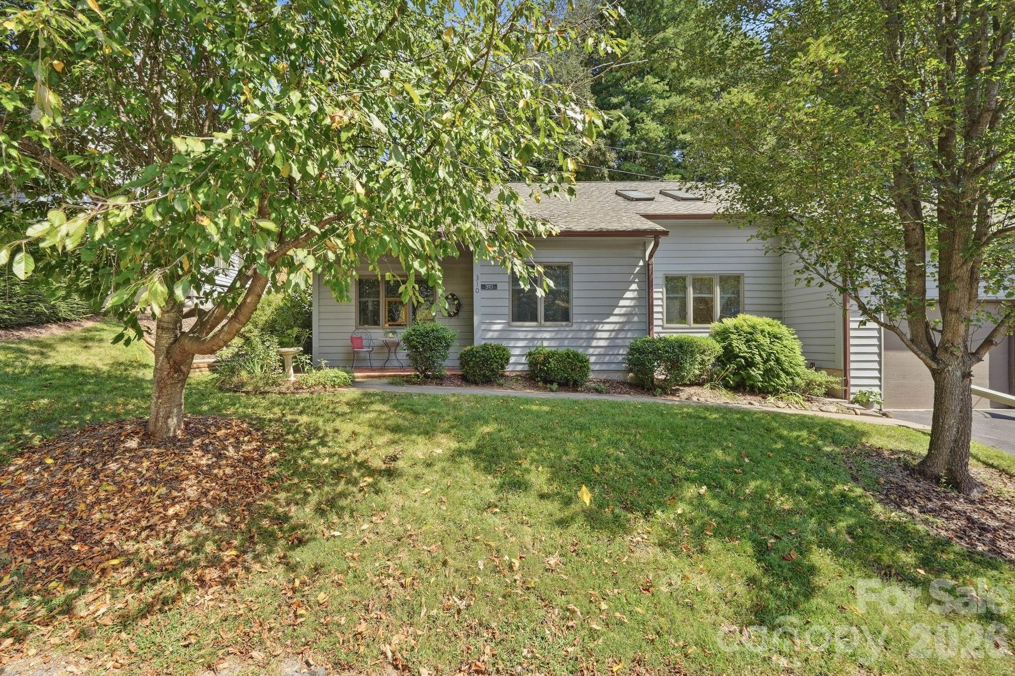 Gray single-story home with a garage, framed by mature trees and a leafy front lawn.
