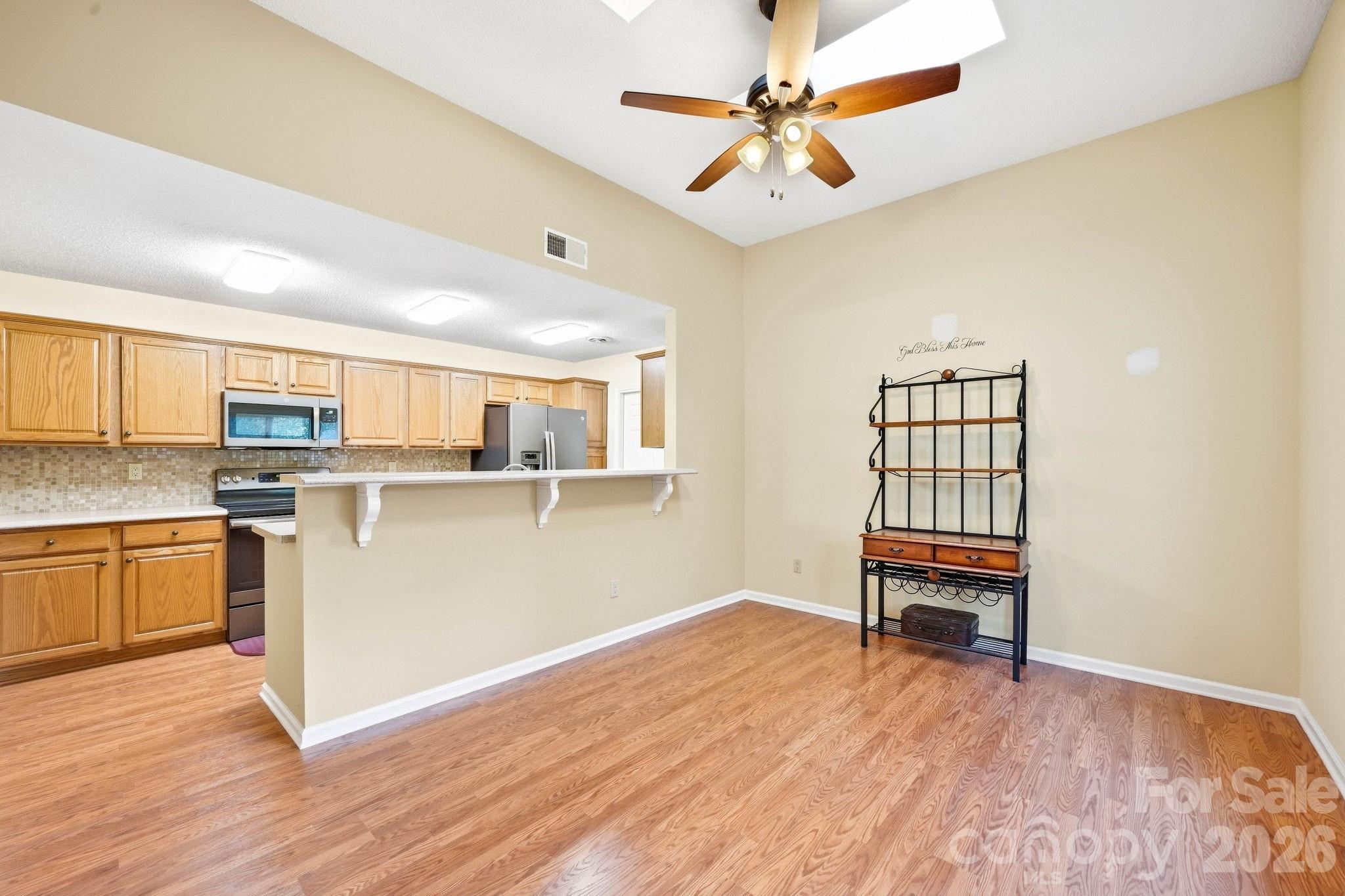 Open dining area with wood-look floors, a breakfast bar, and light wood kitchen cabinets.