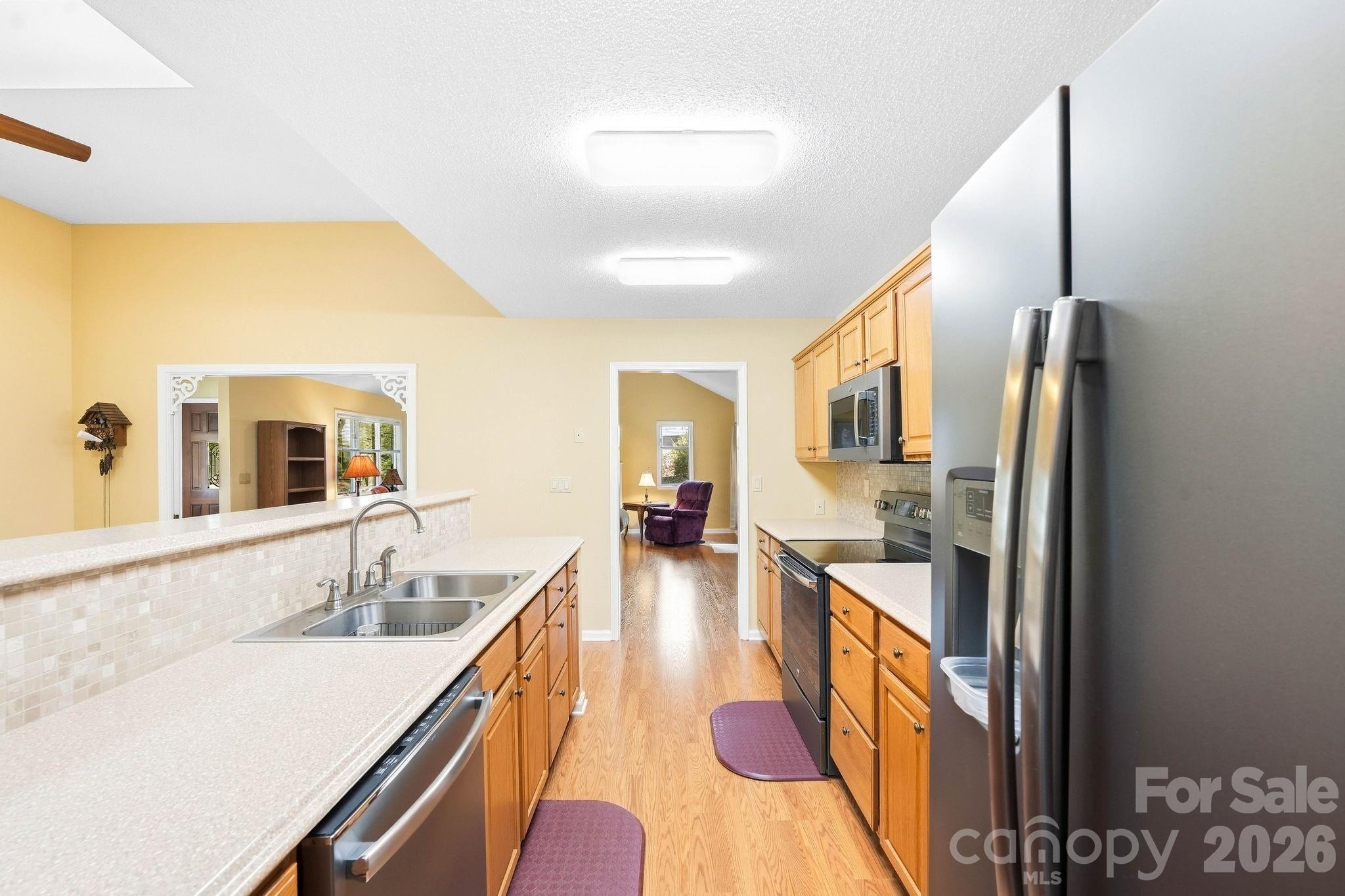 Kitchen with honey-colored cabinets, stainless steel appliances, and a doorway to a sitting room.