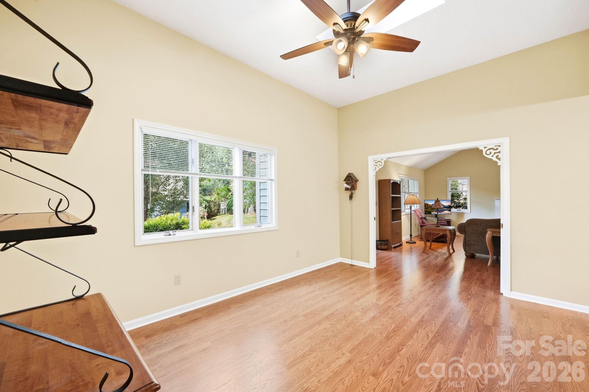 Bright room with hardwood floors, a large window, and an opening to a furnished living room.