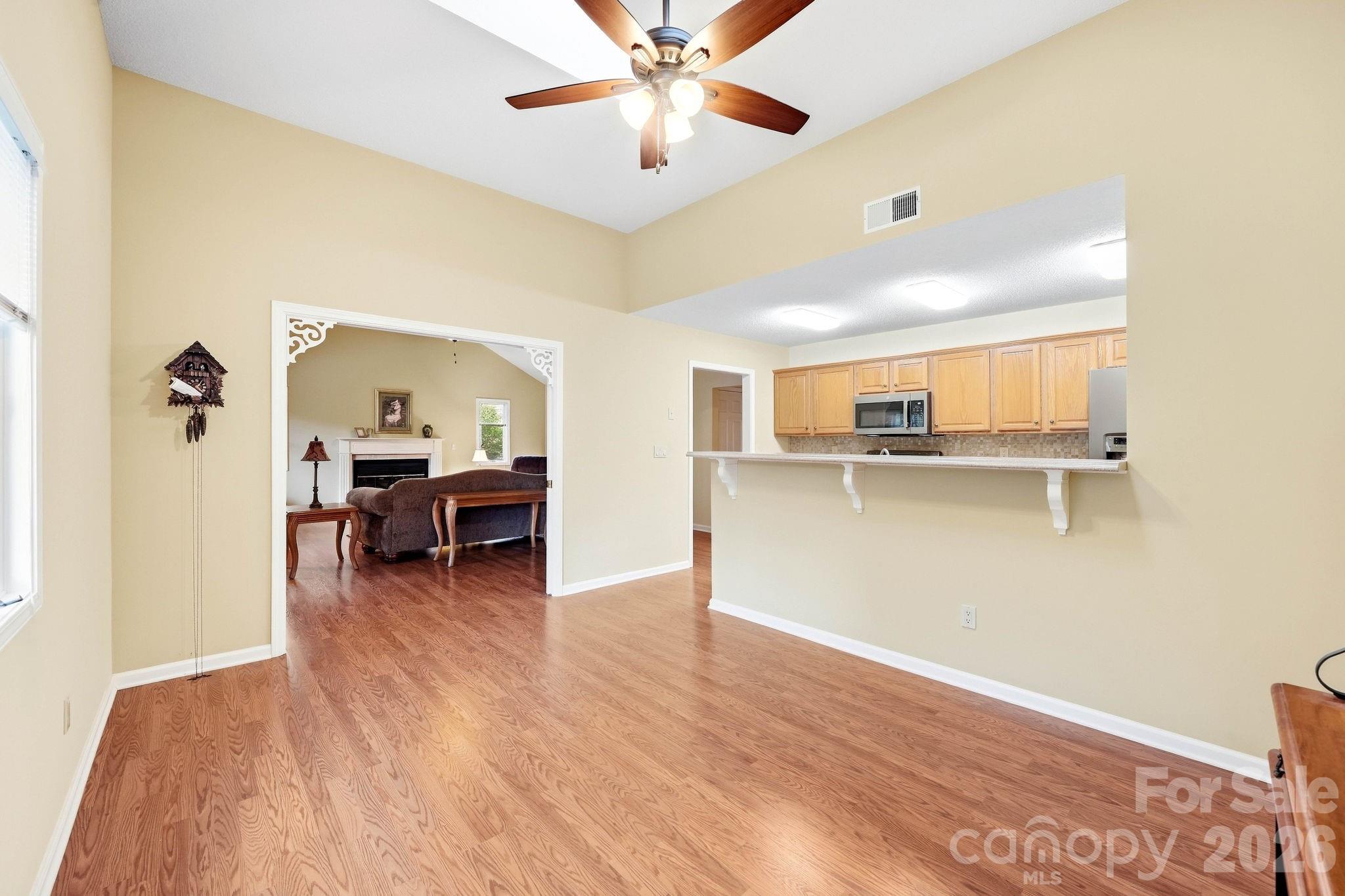 Open dining area and kitchen with wood floors, breakfast bar, and view into a furnished living room.