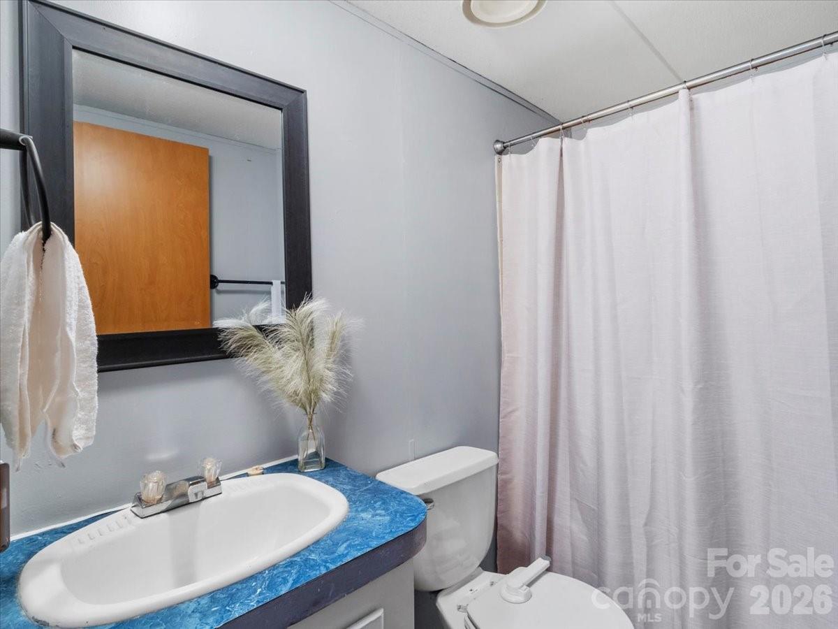 Bathroom with a blue marbled vanity, dark-framed mirror, toilet, and pale shower curtain.