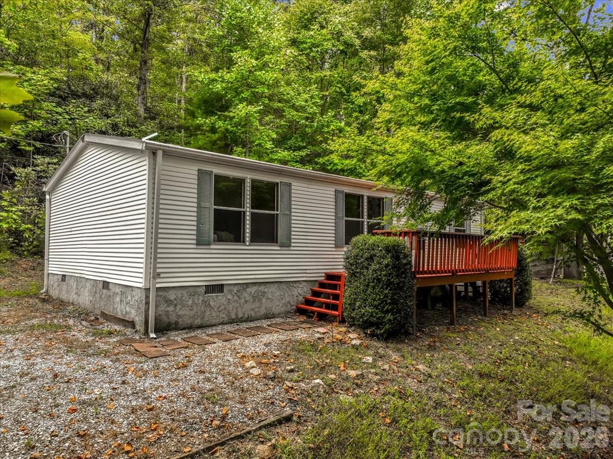 White-sided home with green shutters and a raised wooden deck in a wooded setting.