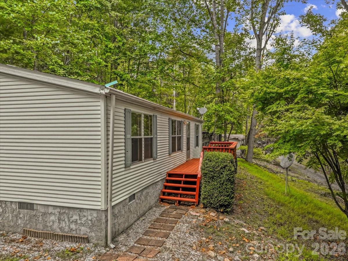 Light-colored manufactured home with orange-red deck steps, surrounded by mature trees.