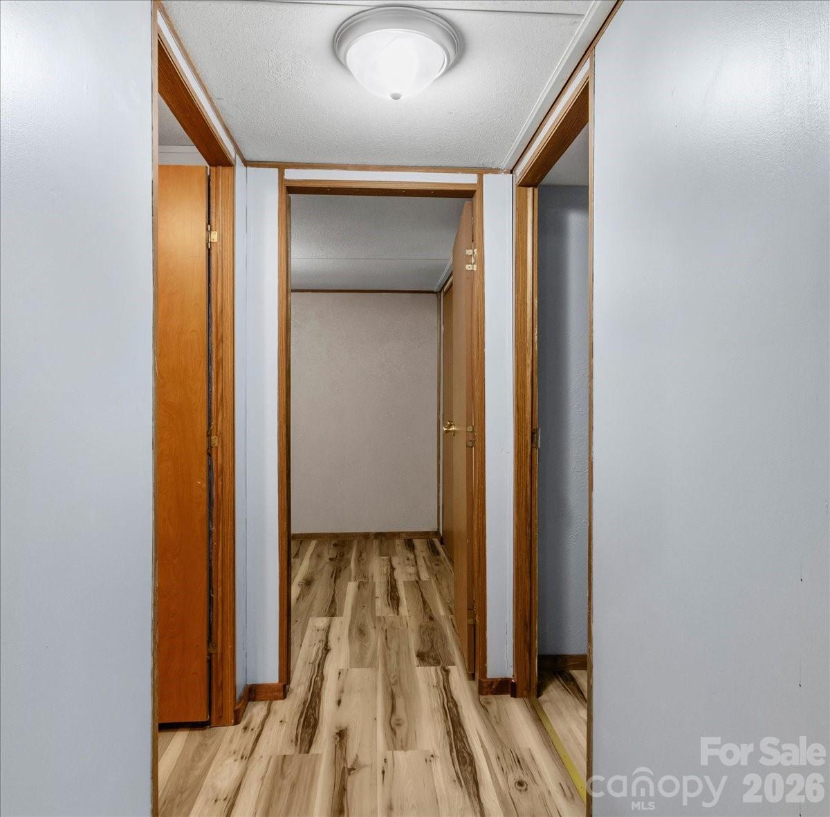 Hallway with wood-look plank flooring, warm wood trim, and several open doorways.