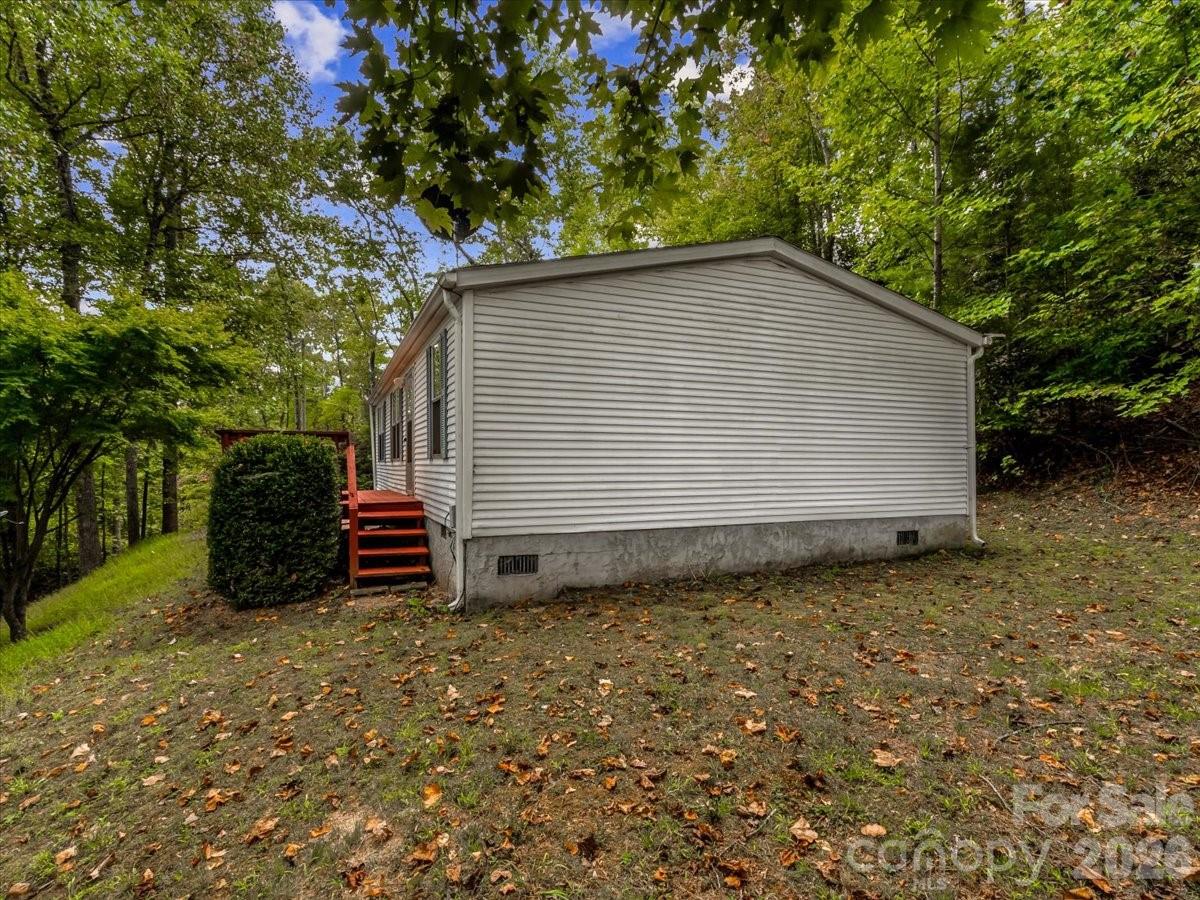 Light-colored manufactured home among trees, with red steps at the side entrance.