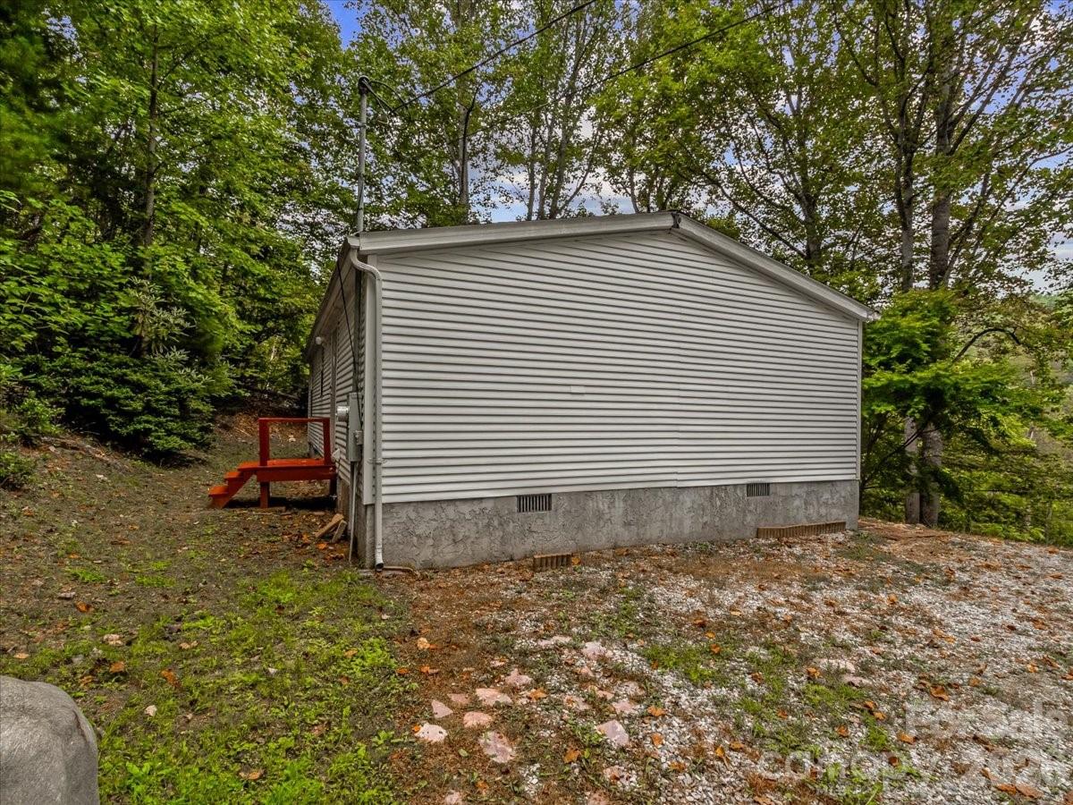 Light-colored home with red steps on a wooded, sloping lot.