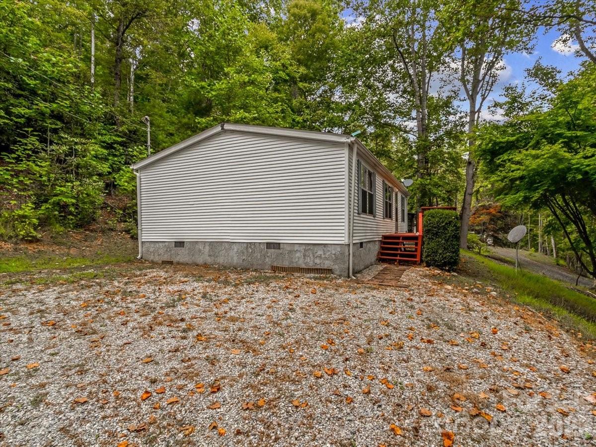 Manufactured home in a wooded clearing with red entrance steps and a gravel yard.