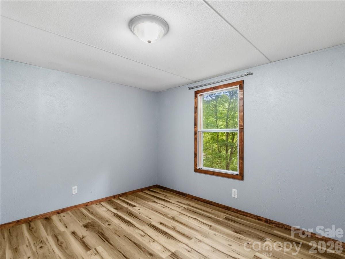 Unfurnished room with wood-look flooring, blue-gray walls, and a window overlooking trees.