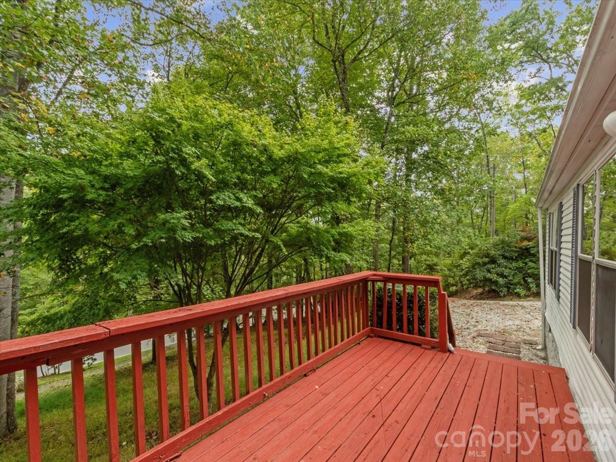 Red wooden deck beside the house, overlooking dense leafy woodland.