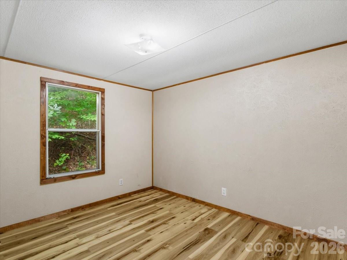 Empty bedroom with wood-look plank flooring, wood-trimmed window, and leafy view outside.