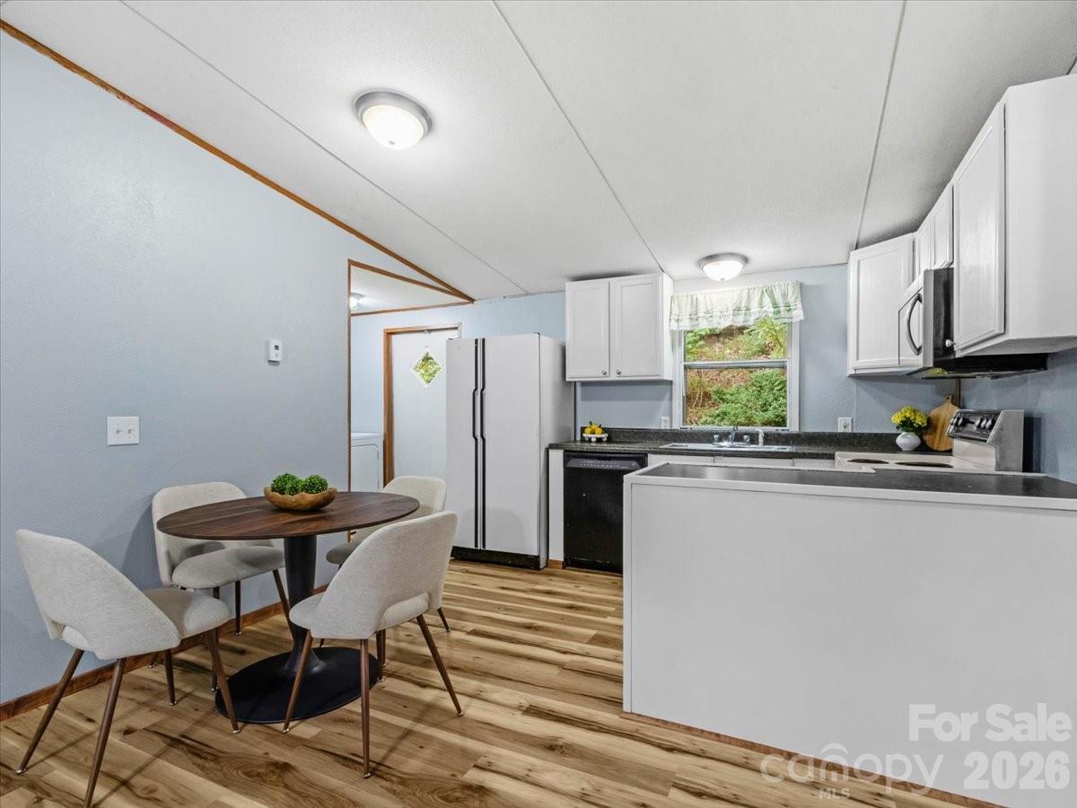 Kitchen with white cabinets and dark countertops beside a round dining table and wood-look flooring.