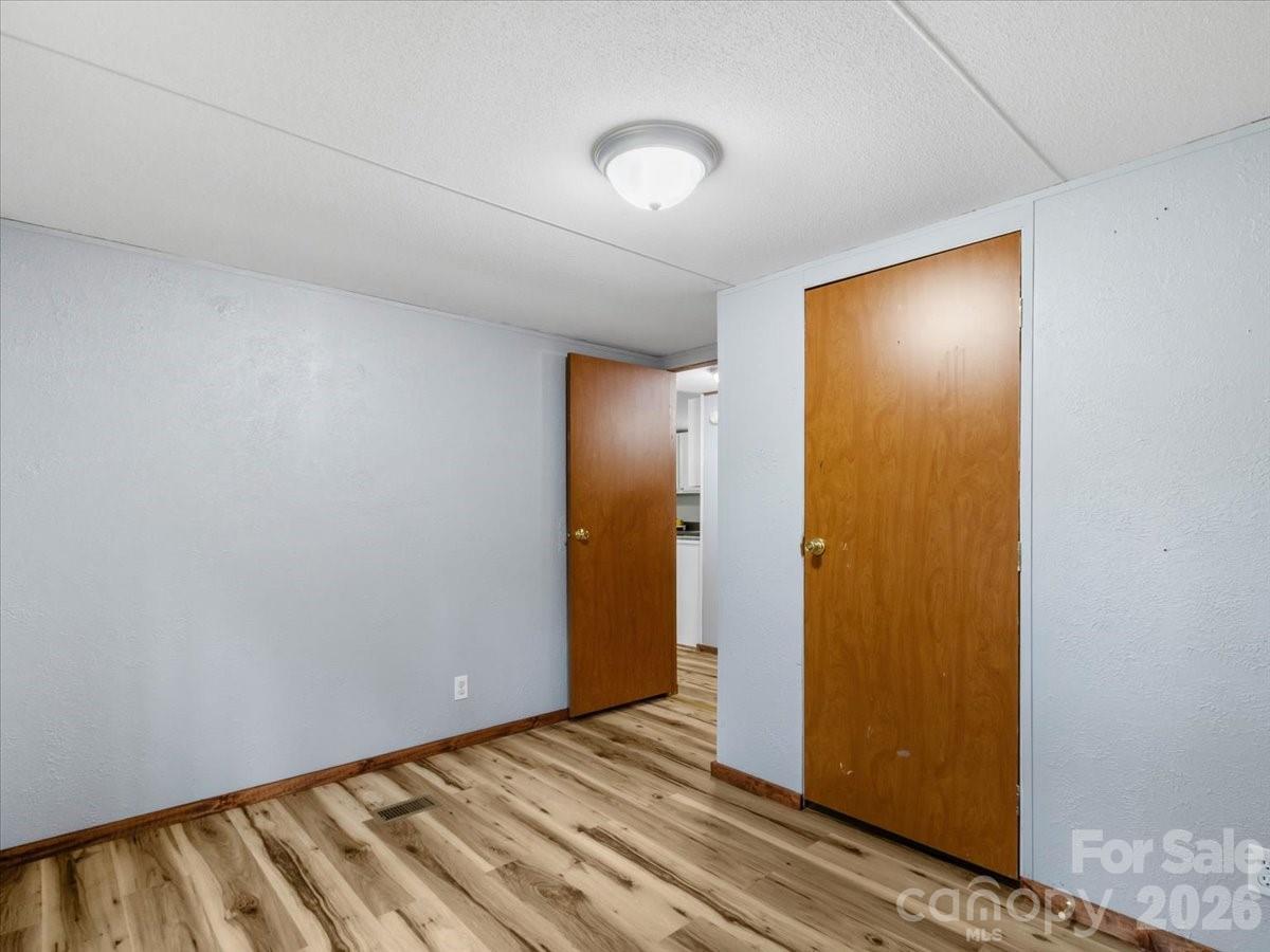 Empty room with wood-look flooring and two wooden doors, one open to an adjoining area.