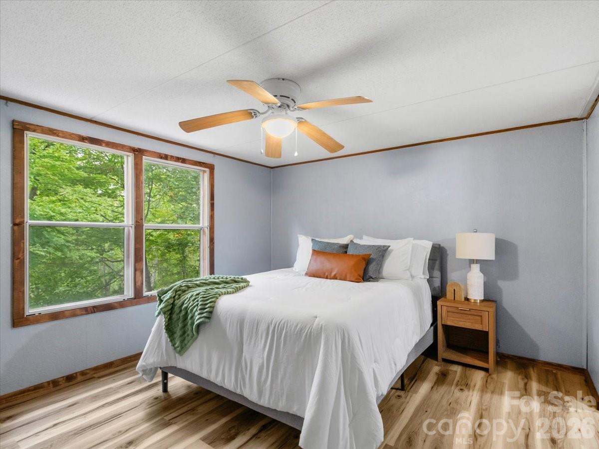 Bedroom with a white bed, green throw, and wood-trimmed windows overlooking trees.