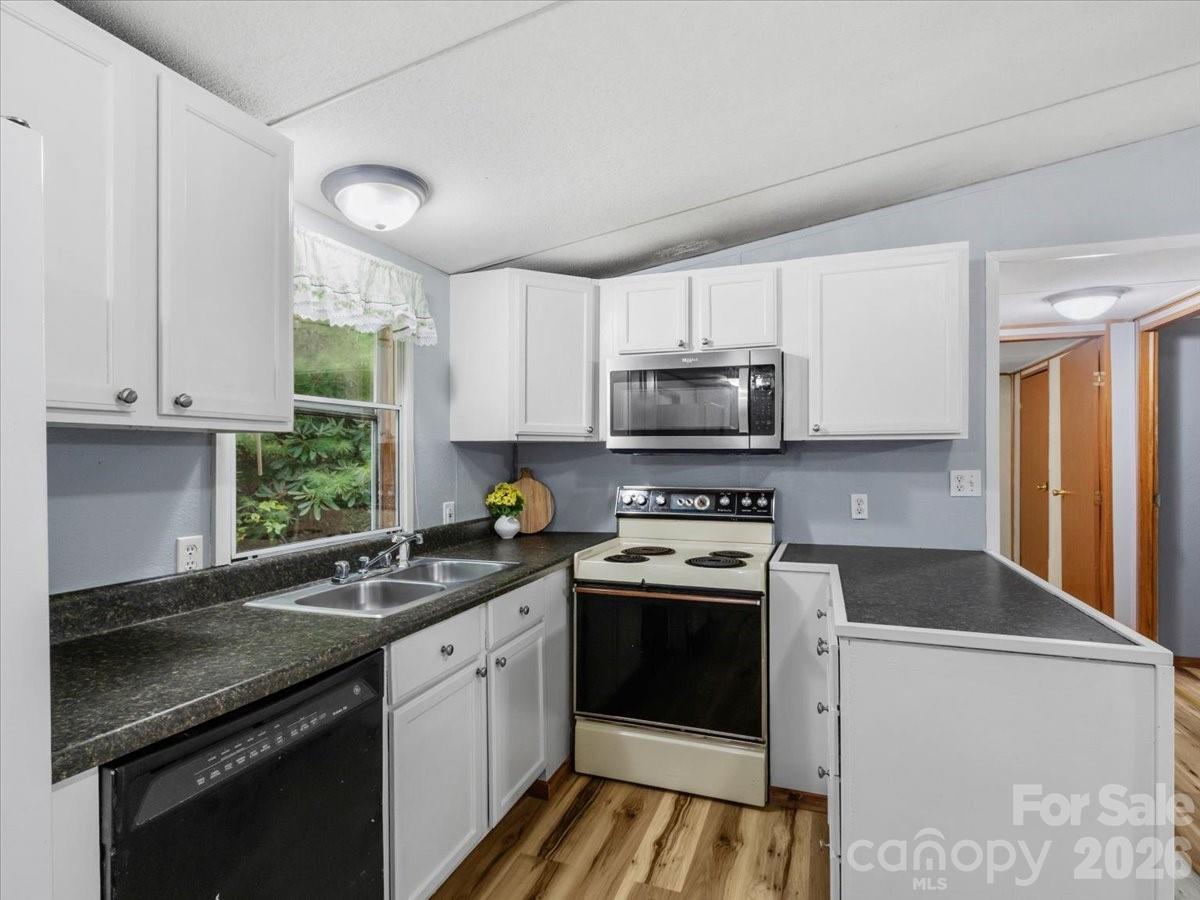 Kitchen with white cabinets, dark countertops, a window over the sink, and an electric range.