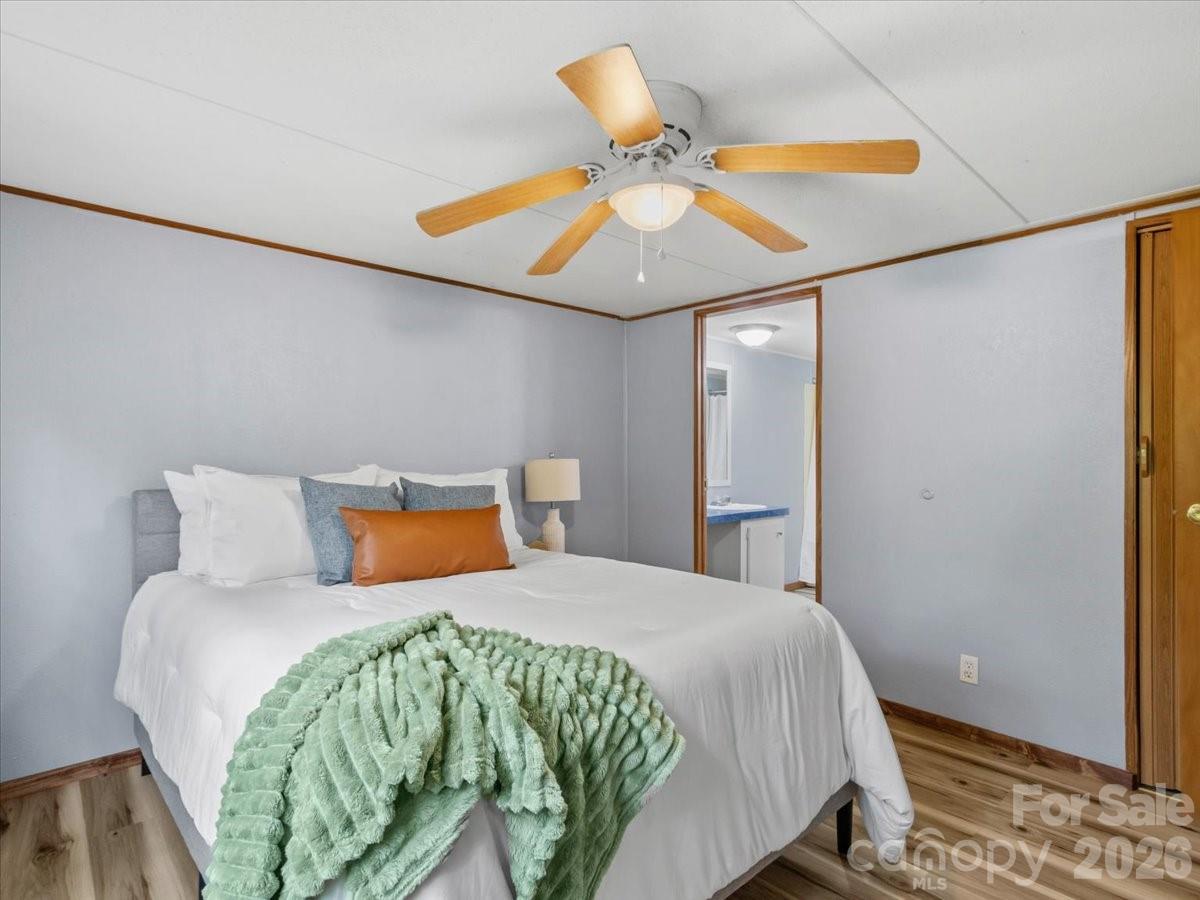 Staged bedroom with a white bed, mint-green throw, wood-blade ceiling fan, and bathroom doorway.