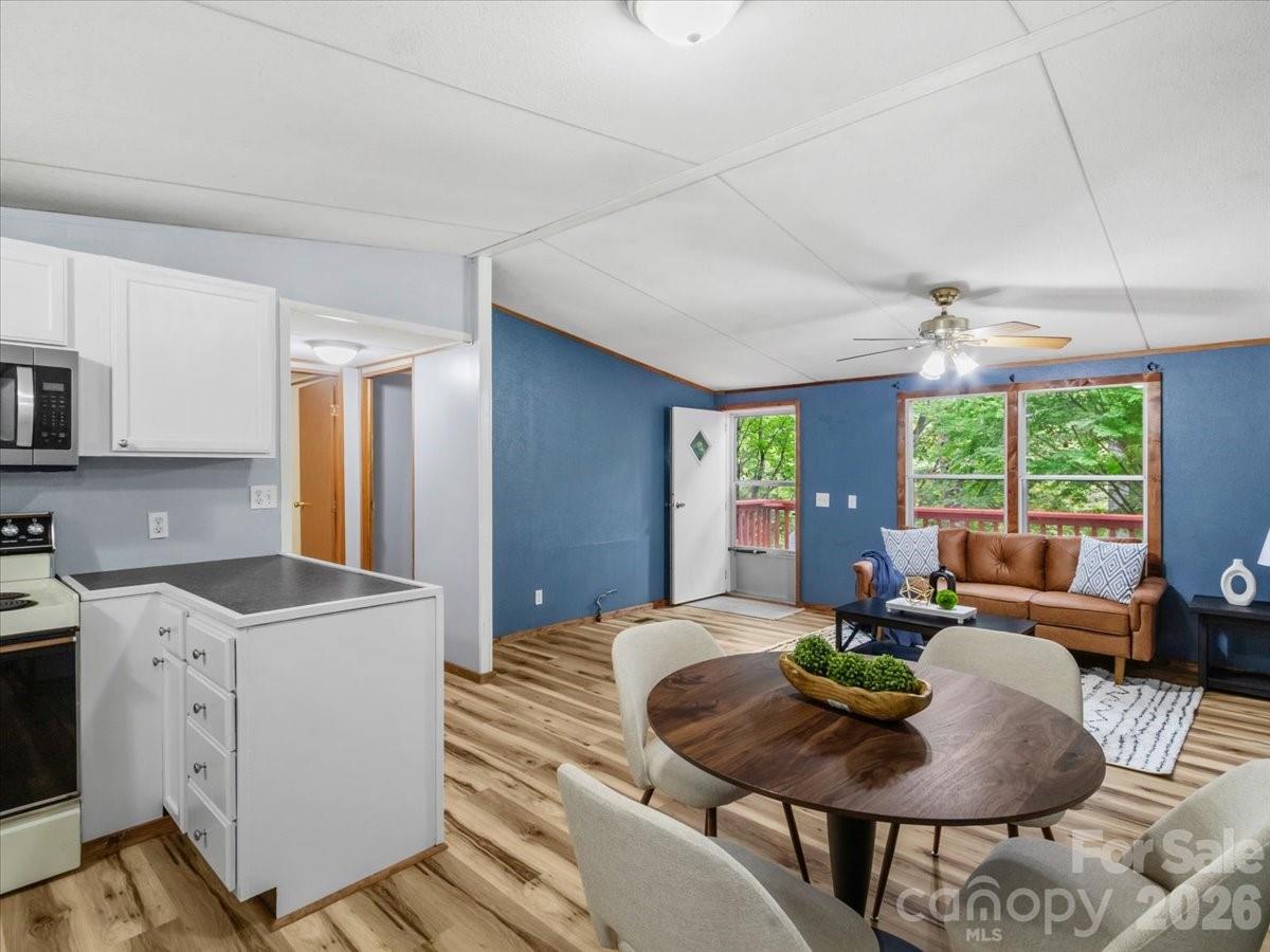 Open-plan kitchen and living area with blue walls, wood-look floors, and windows overlooking trees.