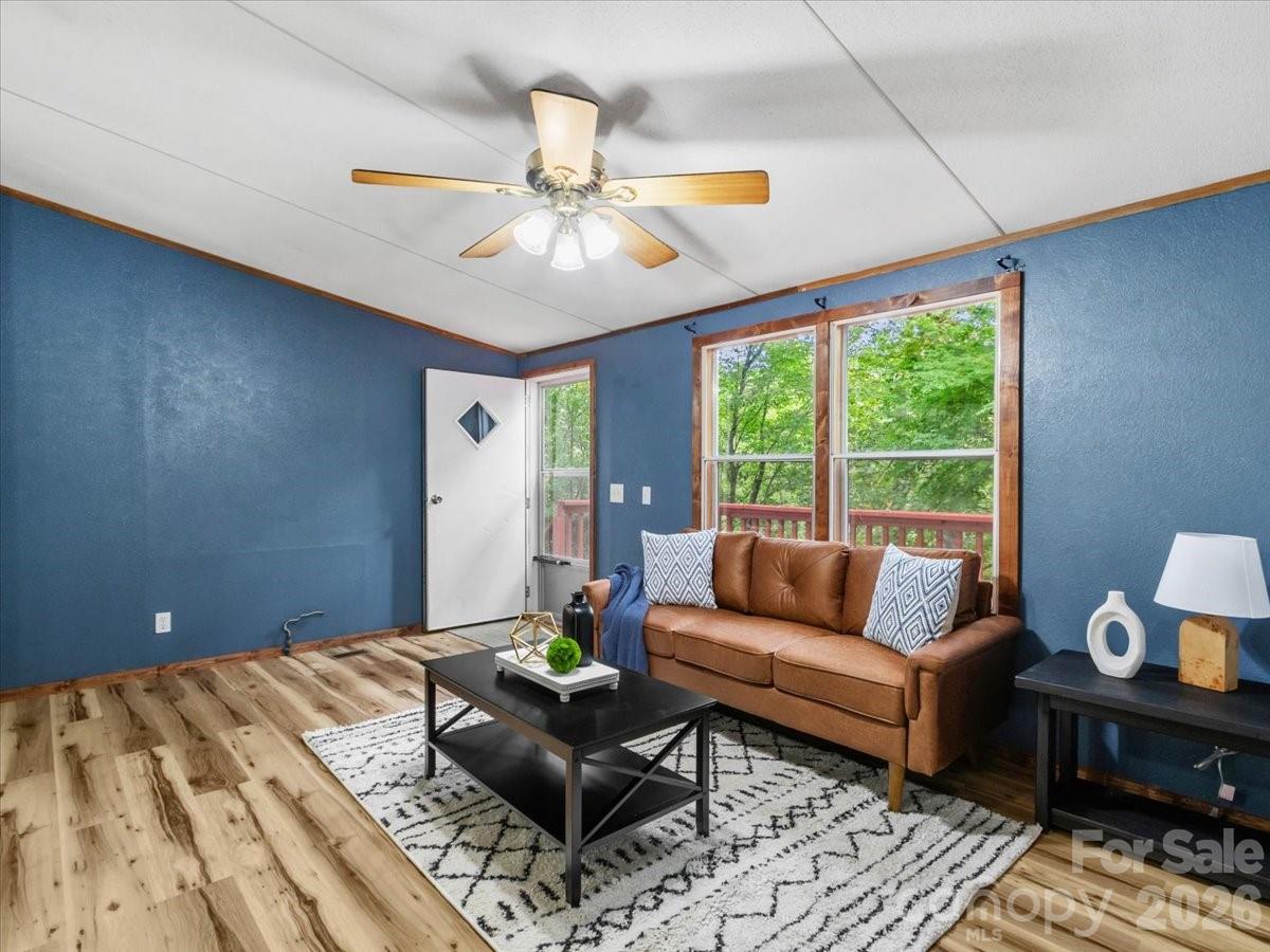 Staged living room with blue walls, brown leather sofa, and large windows overlooking leafy trees.
