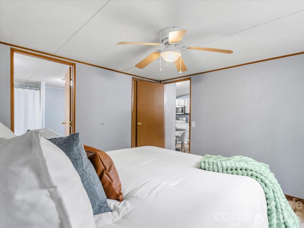 Bedroom with a white bed, mint-green throw, and ceiling fan; open doorways reveal adjoining rooms.