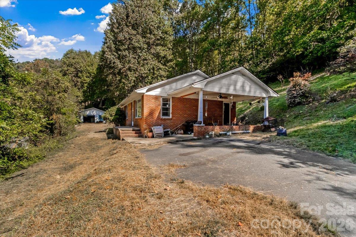 Brick ranch house with a covered porch and driveway, surrounded by trees and a sloping yard.