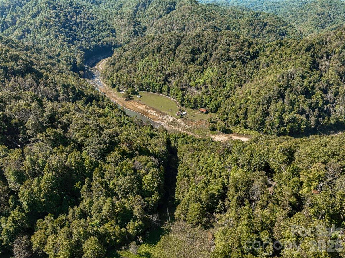 Aerial view of a forested property with a creek, a long clearing, and scattered small buildings.