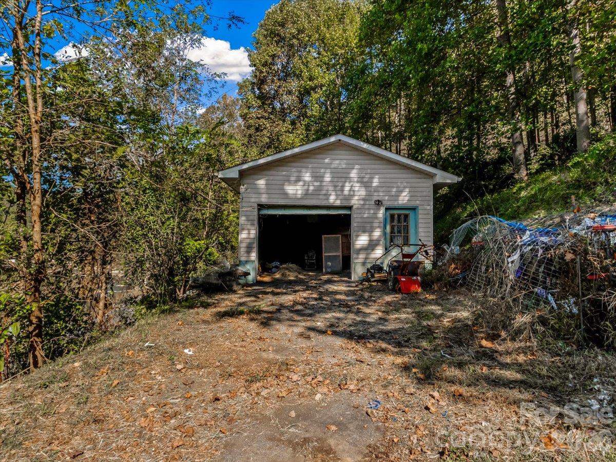 Detached gray garage with open bay and blue-trimmed door on a wooded lot.