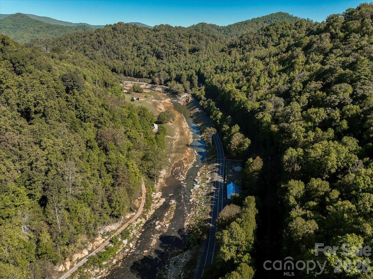 Aerial view of a wooded river valley with a rocky creek and winding road.